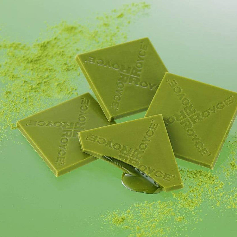 ROYCE' Chocolate - Prafeuille Chocolat Matcha - Image shows green chocolate squares filled with green sauce and engraved with the words ROYCE. Accents include green tea powder scattered. Background is in green color.
