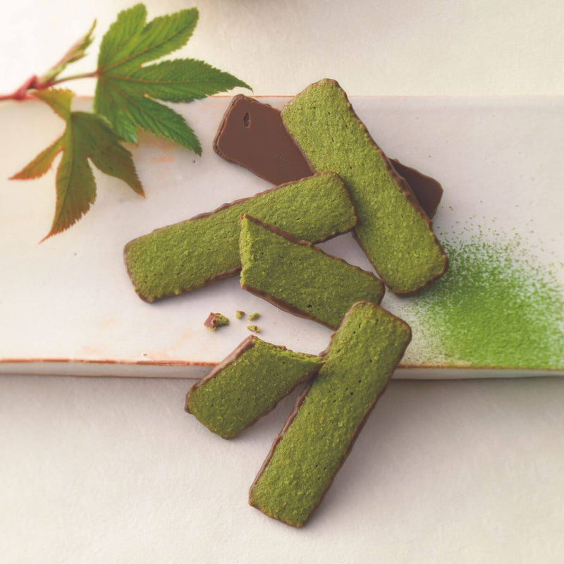 ROYCE' Chocolate - Baton Cookies Matcha (25 Pcs) - Image shows green cookies coated with brown chocolate on a white plate with green tea powder and some leaves for props.